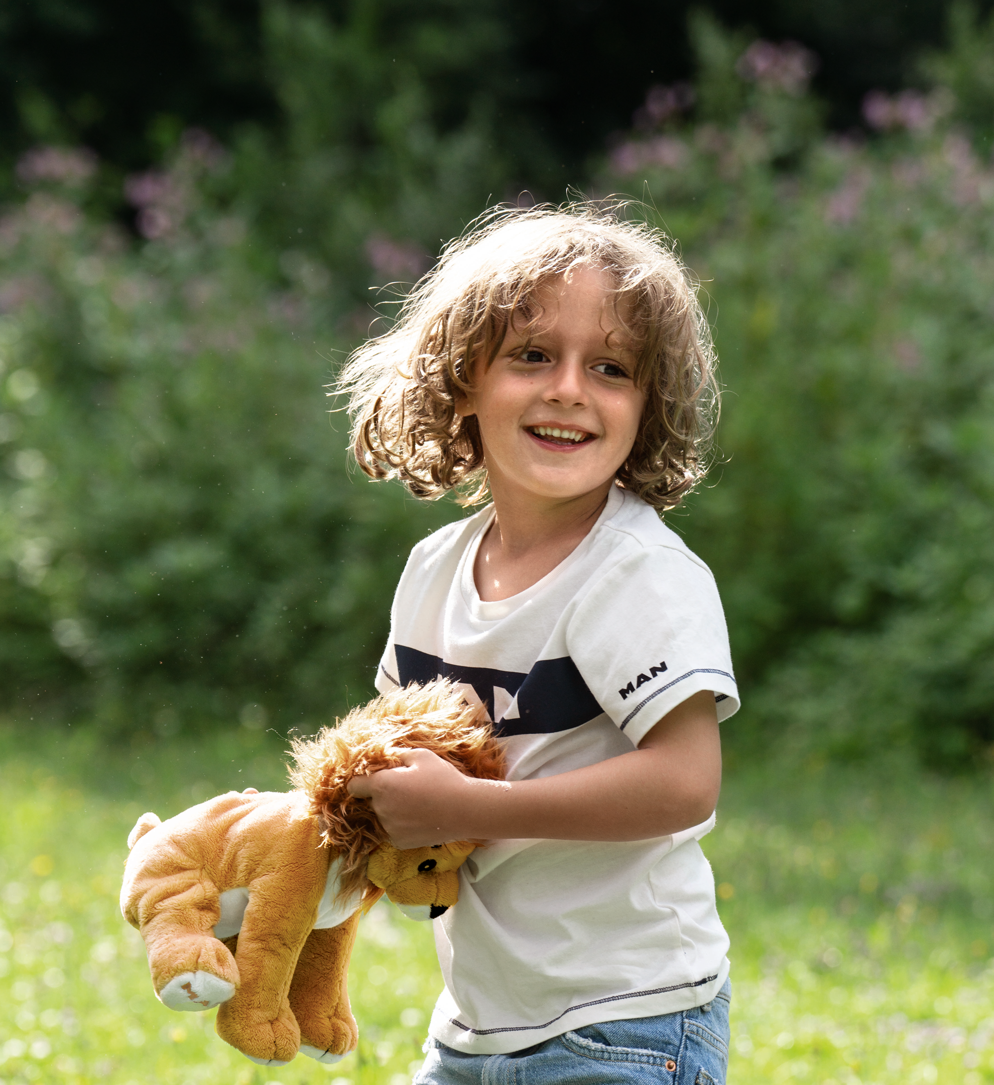 Fröhliches Kind in einem MAN-T-Shirt hält ein Löwen-Plüschtier, ideal für spielerische und aktive Momente im Freien.