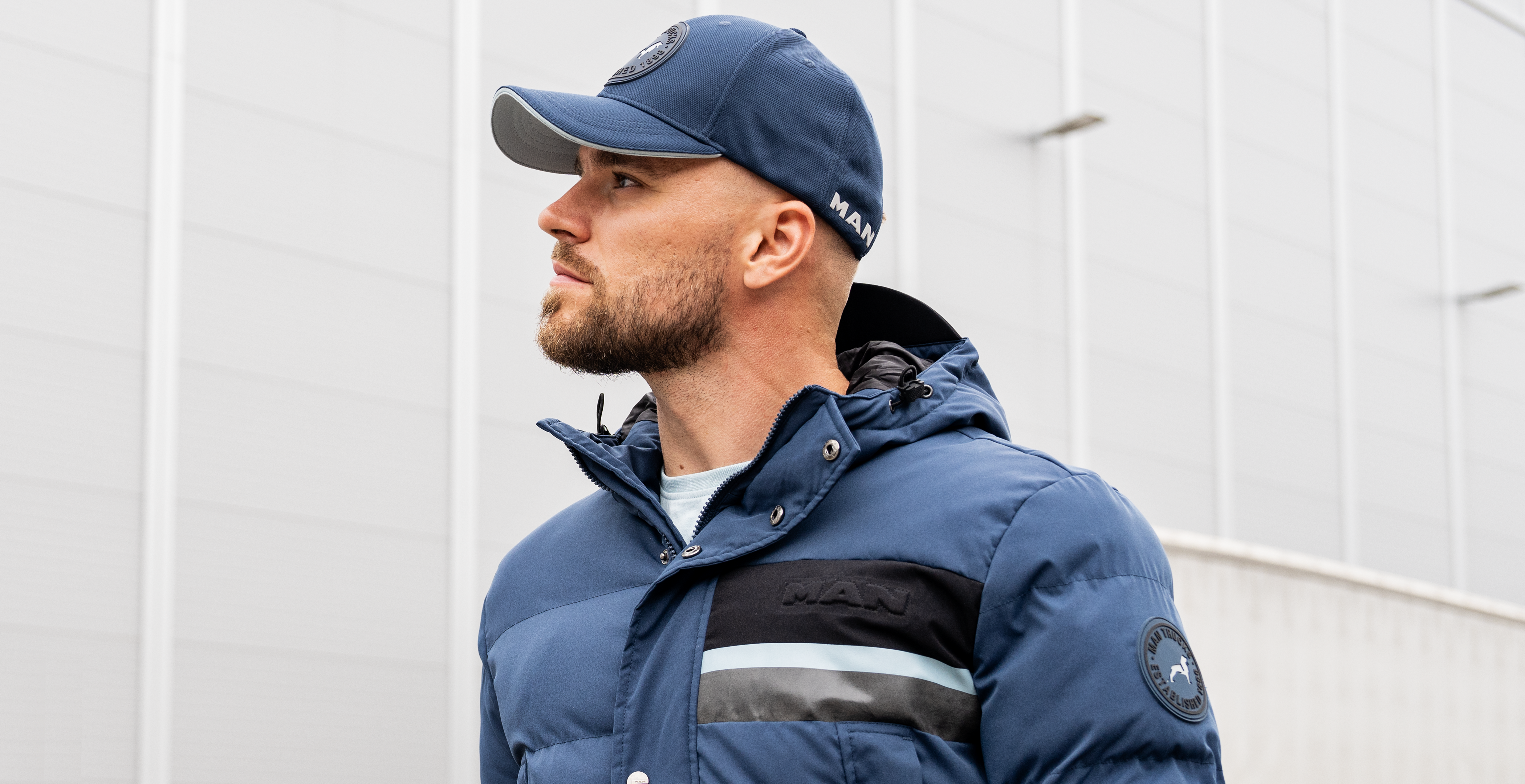 Mann trägt eine blaue Jacke und Cap aus der MAN Lion Collection, ideal für einen modernen, sportlichen Look im Freien.