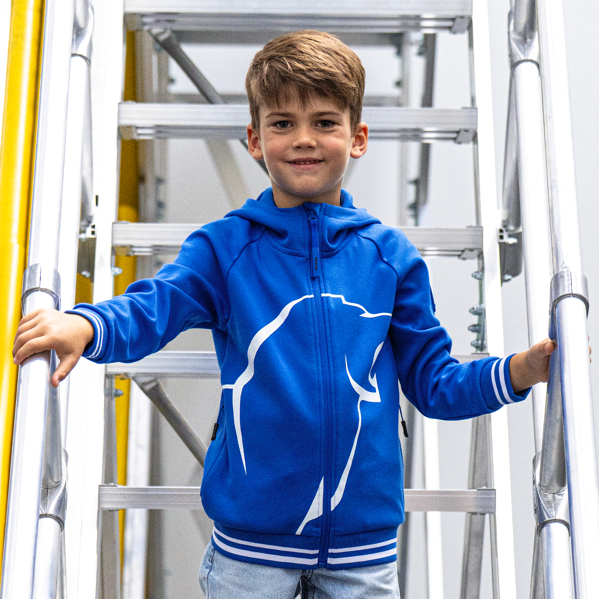 Junge in blauer MAN-Kinder-Kapuzenjacke mit weißem MAN Löwen-Print und gestreiften Bündchen