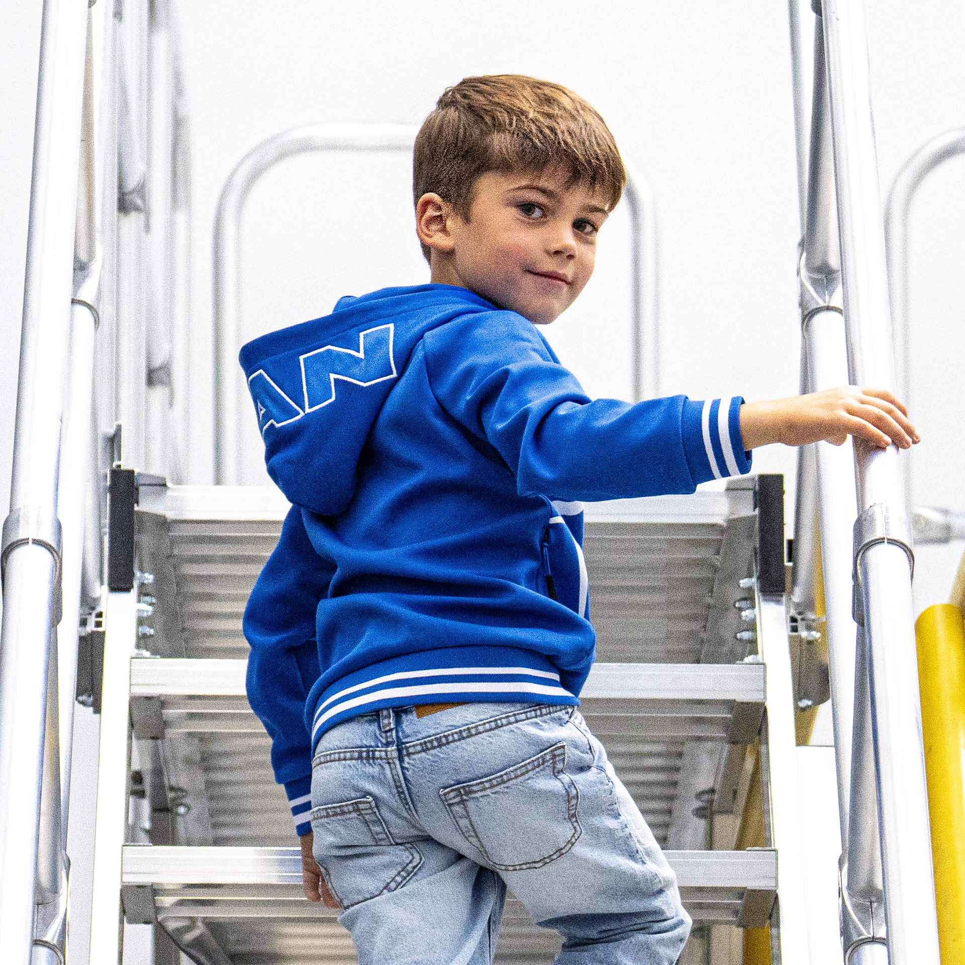 Junge auf einer Treppe in blauer MAN-Kinder-Kapuzenjacke mit MAN-Print auf der Kapuze
